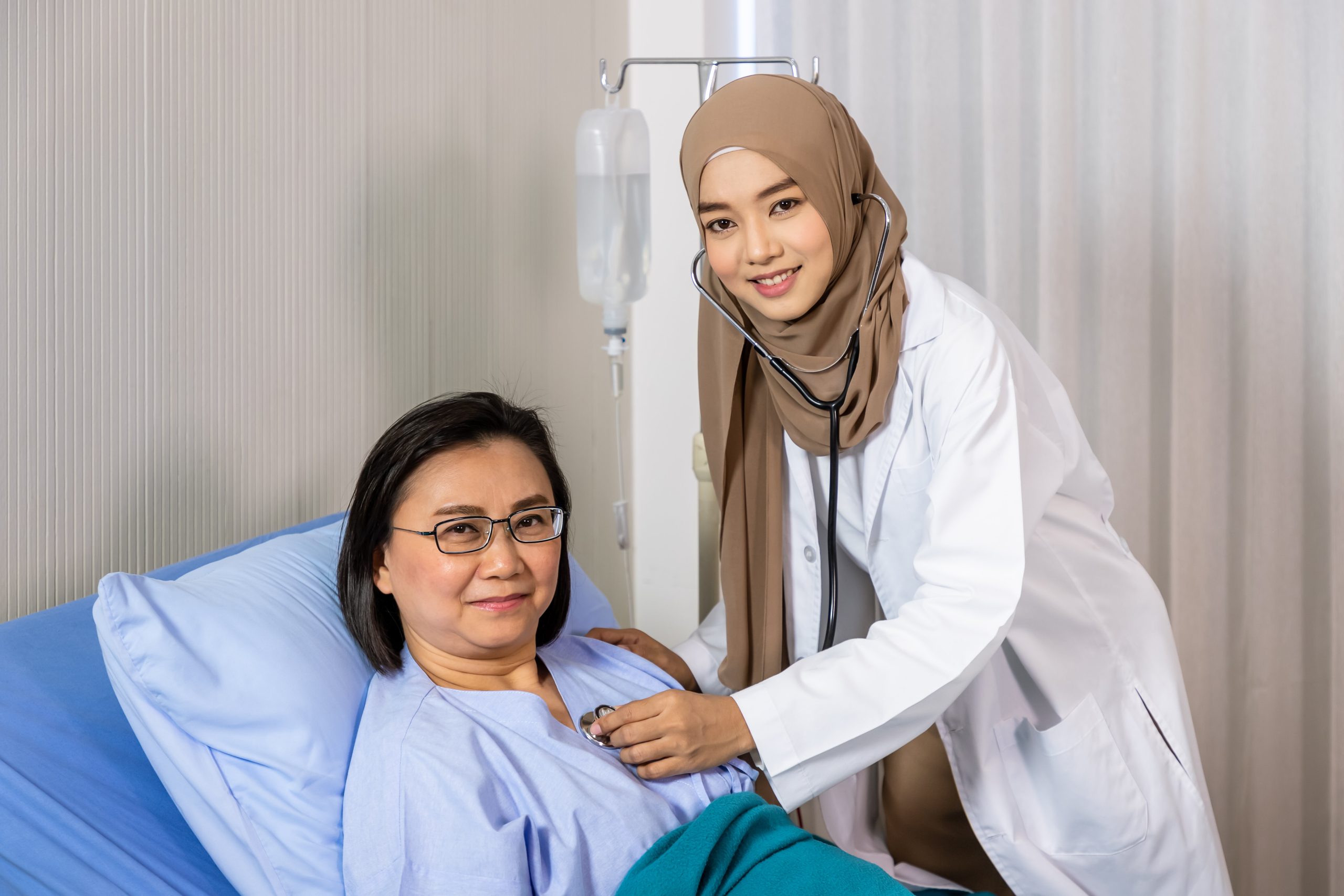 muslim-female-woman-medical-doctor-using-stethoscope-listen-heartbeat-patient-lying-bed-looking-camera (1)